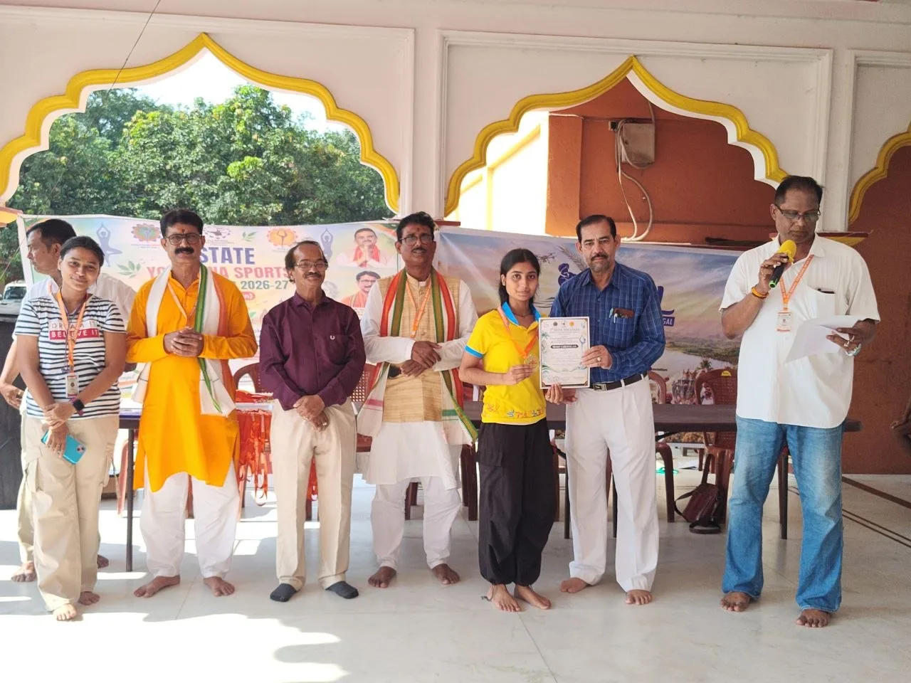 Officials stand with an athlete in blue as a certificate is held in the hall.